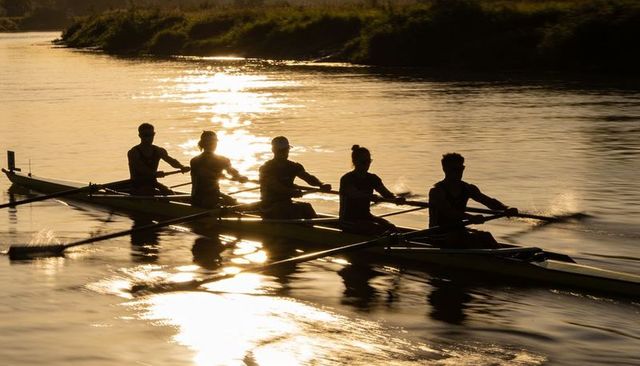 Sunset rowing crew gliding in racing shell silhouette emphasizing teamwork and motion