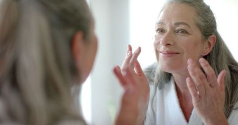 Mature Woman Applying Makeup with Delightful Smile in Bright Room - Download Free Stock Images Pikwizard.com