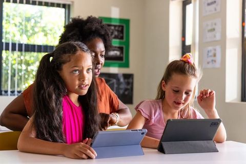 African american teacher guiding two girls on tablets for collaborative classroom learning