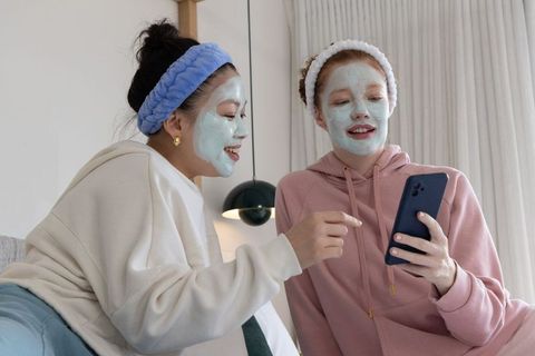 Multicultural friends wearing face masks and hoodies sharing skincare tips on smartphone