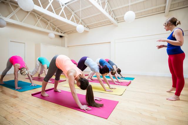 Trainer assisting group of people with downward dog pose yoga exercise in the fitness studio