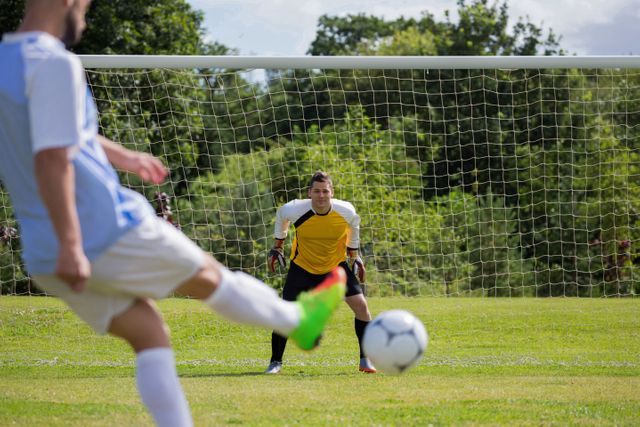 Soccer player in white and blue uniform kicking ball towards goal with focused goalkeeper ready to block. Perfect for articles on sports strategies, team dynamics, athletic training, or promoting soccer events and equipment.