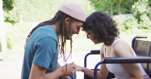 Biracial couple touching heads holding hands in garden, woman in wheelchair, man with dreadlocks. wellbeing and domestic lifestyle with physical disability.