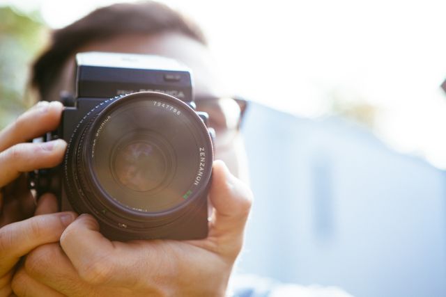 Photographer holding camera, focusing lens while taking shot in outdoor setting. Ideal for use in articles focused on photography, camera equipment reviews, tutorial videos, visual storytelling, and promoting photography workshops or courses.