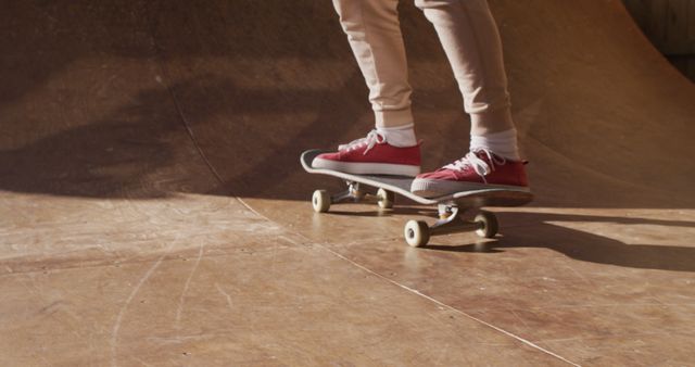 Someone wearing red sneakers is balancing on a skateboard at a skatepark. The close-up shot focuses on the legs and feet, highlighting the skateboard. This image can be used for promoting outdoor activities, skateboarding lessons, athletic shoes, or sportswear brands.