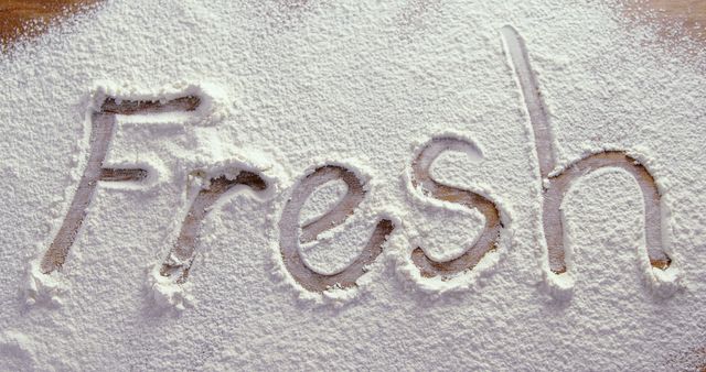 The word Fresh is written in a dusting of white flour on a wooden surface, with copy space. It evokes a sense of cleanliness and purity, often associated with cooking and baking.