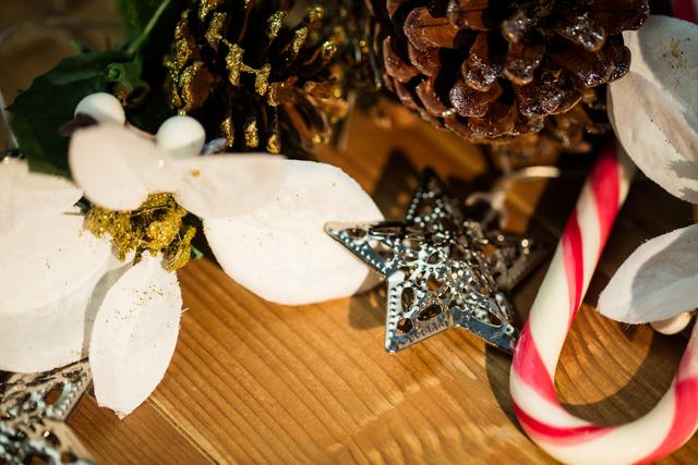 Close-up of Christmas decorations arranged on a wooden surface, featuring a candy cane, star ornament, pinecones, and white flowers. Ideal for Christmas cards, holiday announcements, festive website banners, and seasonal blog posts.