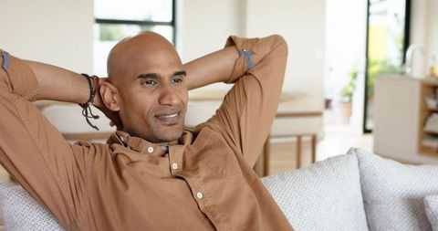 Relaxing mature man reclining on sofa in bright modern living room with neutral decor