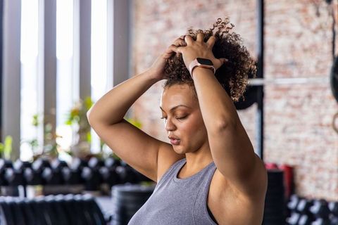 African american woman tying curly hair before workout in industrial gym