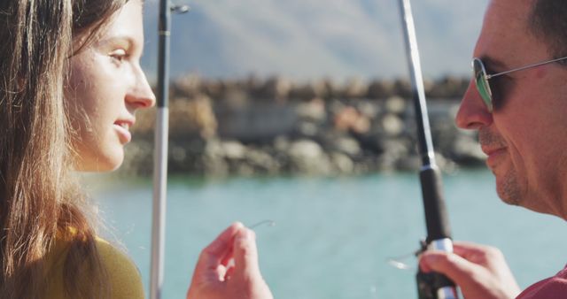 Happy caucasian teenage daughter listening to father teaching her fishing in harbour on a sunny day. Leisure, free time, hobbies, family, travel and vacations.
