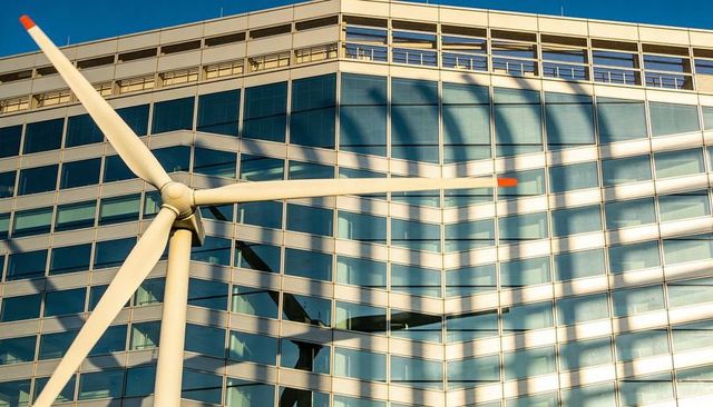 Wind turbine rotor casting shadows on curved glass office with orange blade tips