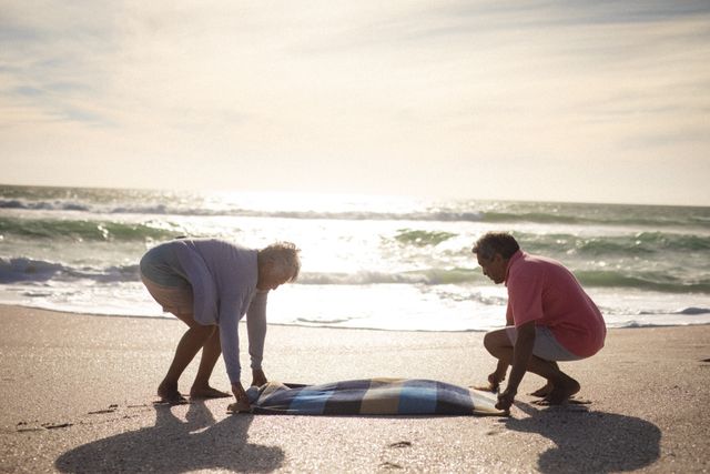 Full length side view of senior couple laying blanket together on shore at beach - Download Free Stock Photos Pikwizard.com