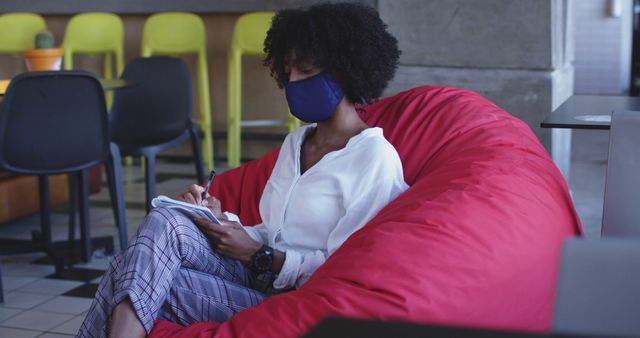 Woman Writing in Notebook While Sitting on Red Beanbag in Modern Workspace - Download Free Stock Images Pikwizard.com