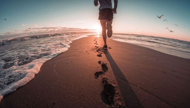 Runner on serene beach leaving footprints during sunset