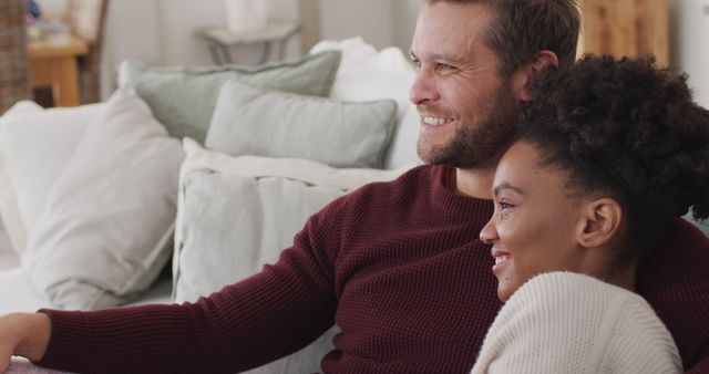 Image of happy diverse couple watching tv on sofa. Love, relationship and spending quality time together at home.