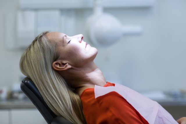 Woman sitting comfortably on a dentist chair in a dental clinic. She appears relaxed, suggesting a positive dental experience. Ideal for use in healthcare promotions, dental clinic advertisements, oral hygiene campaigns, and patient care brochures.