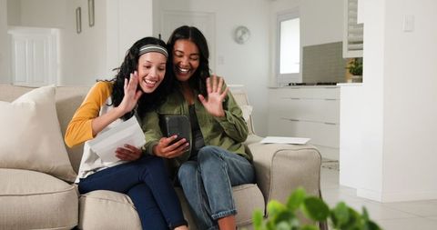 Two african american women relaxing and enjoying a smartphone couch conversation