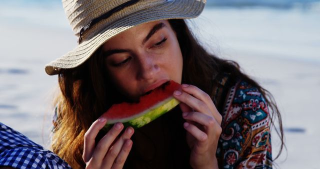 Caucasian woman wearing sunhat eating watermelon in the sun at beach. Free time, summer and vacations, unaltered.
