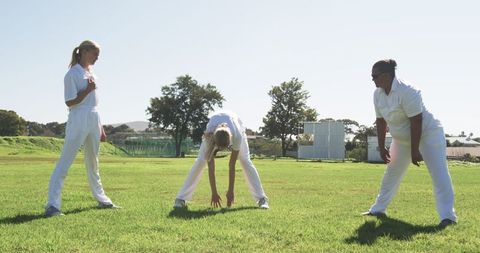 Female Athletes Stretching on Grassy Field in Sunlight
