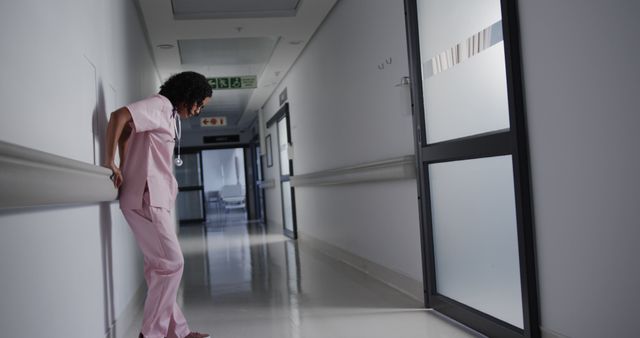 Exhausted biracial female doctor leaning on wall in hospital. Medicine, healthcare, despair and hospital, unaltered.
