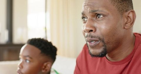 African american father watching game with son on sofa conveying focused family moment