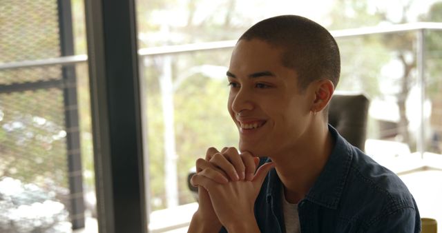 Smiling Young Person with Hands Clasped, Sitting by Window - Download Free Stock Images Pikwizard.com