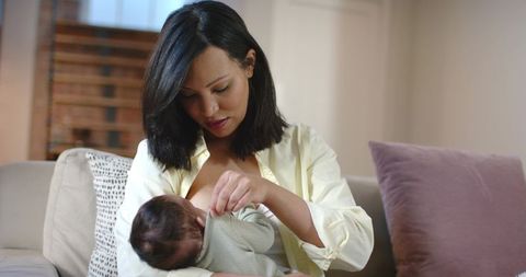 Mother breastfeeding baby on cozy sofa at home