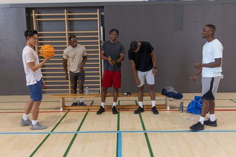 Multiracial men chatting and warming up with basketball on indoor court bench camaraderie