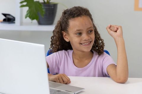 Young girl celebrating success while using laptop at desk, remote learning concept
