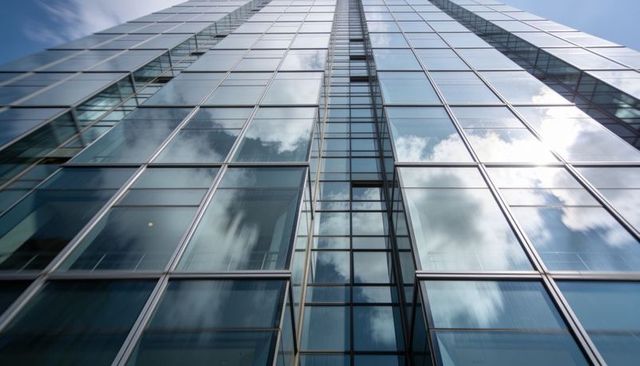 Rising glass skyscraper with mirrored facade reflecting clouds and sunlit glare