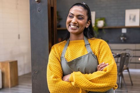 Confident indian barista leaning on wood post in cozy rustic cafe
