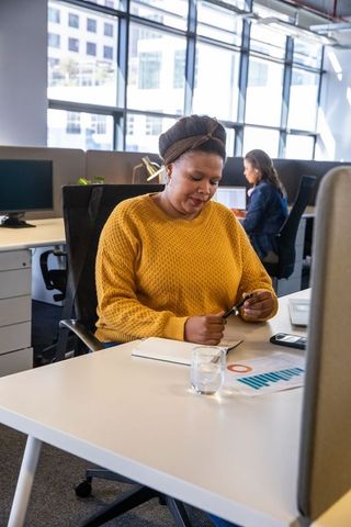 Woman working at modern open-plan office desk holding pen and notebook with charts
