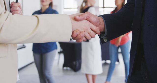Businesspeople wearing professional attire shaking hands in modern office space, signifying successful deal or agreement. Suitable for illustrating concepts like partnerships, business deals, teamwork, and professional connections.