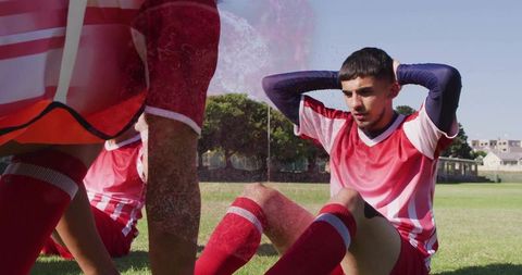Young Soccer Player in Red Kit Doing Sit-Ups on Field