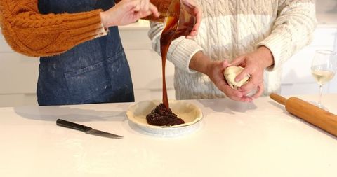 Couple making homemade pie together pouring caramel filling into pastry shell