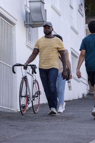 African american man walking white road bicycle down narrow stucco alley with commuters