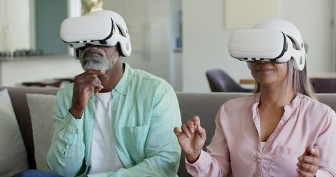 Mature diverse couple experiencing virtual reality together at home with white VR headsets
