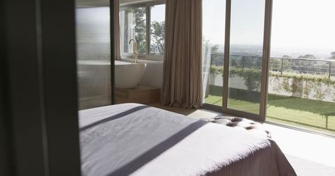 Sunlight pouring through sliding doors onto king bed and oval tub in minimalist bedroom