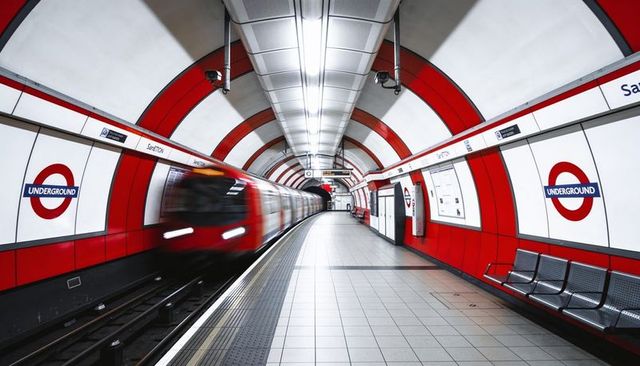 Blurred red train racing through curved london underground tunnel with roundel signs