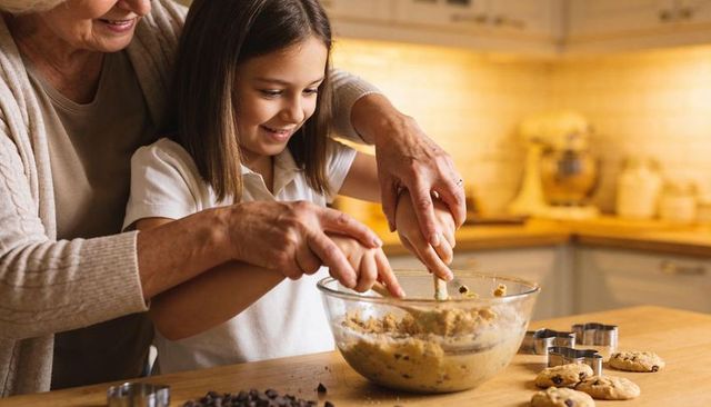 Grandmother guiding granddaughter mixing cookie dough in cozy home kitchen
