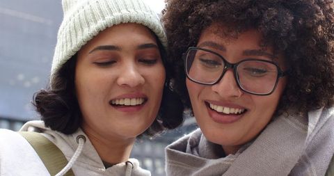 Two friends sharing a laugh while looking down in urban winter closeup