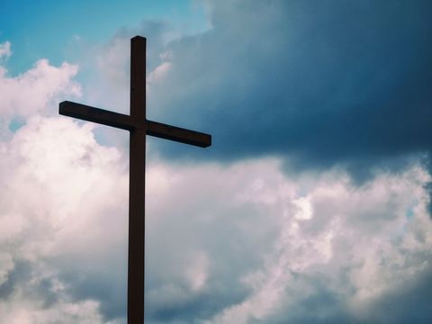 Silhouette of Wooden Cross Against Blue Sky with Clouds