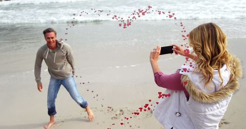 Happy Couple Capturing Memories at Beach with Heart Overlay