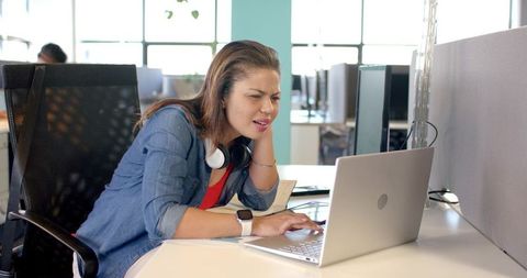 Concentrating woman working on laptop at modern open-plan office desk