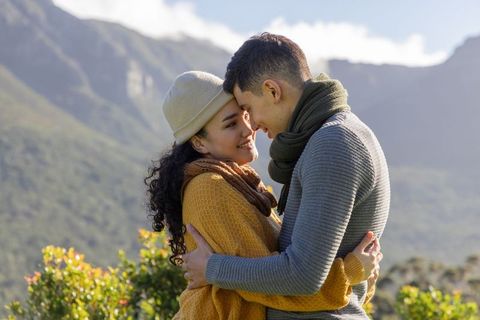 Couple embracing and pressing foreheads in sunlit mountain valley wearing knit cozy layers