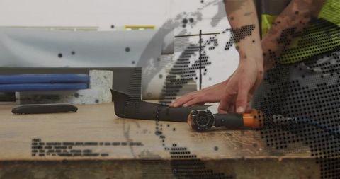 Hands trimming foam strip with rotary grinder on workbench, workshop fabrication closeup