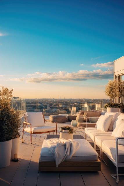 This elegant rooftop lounge offers a luxurious outdoor seating area with comfortable furniture and potted plants. The cityscape view at sunset adds a serene and picturesque ambiance. Perfect for marketing materials targeting luxury real estate, outdoor furniture, travel magazines, or lifestyle blogs that highlight urban living and relaxation.
