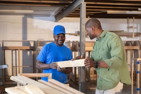 African american carpenters collaborating over wood plank inspecting quality in workshop