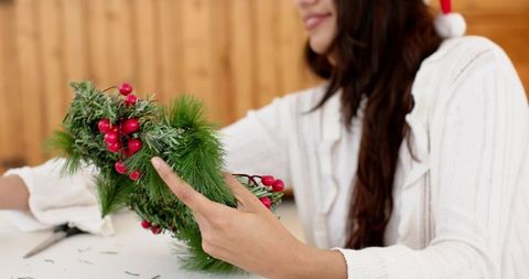 Indian woman crafting festive pine wreath with red berries at cozy holiday workshop