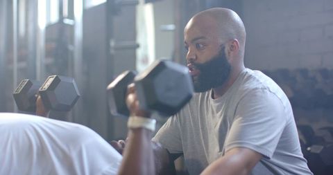 African American Trainer Spotting Client Pressing Hex Dumbbells on Flat Bench